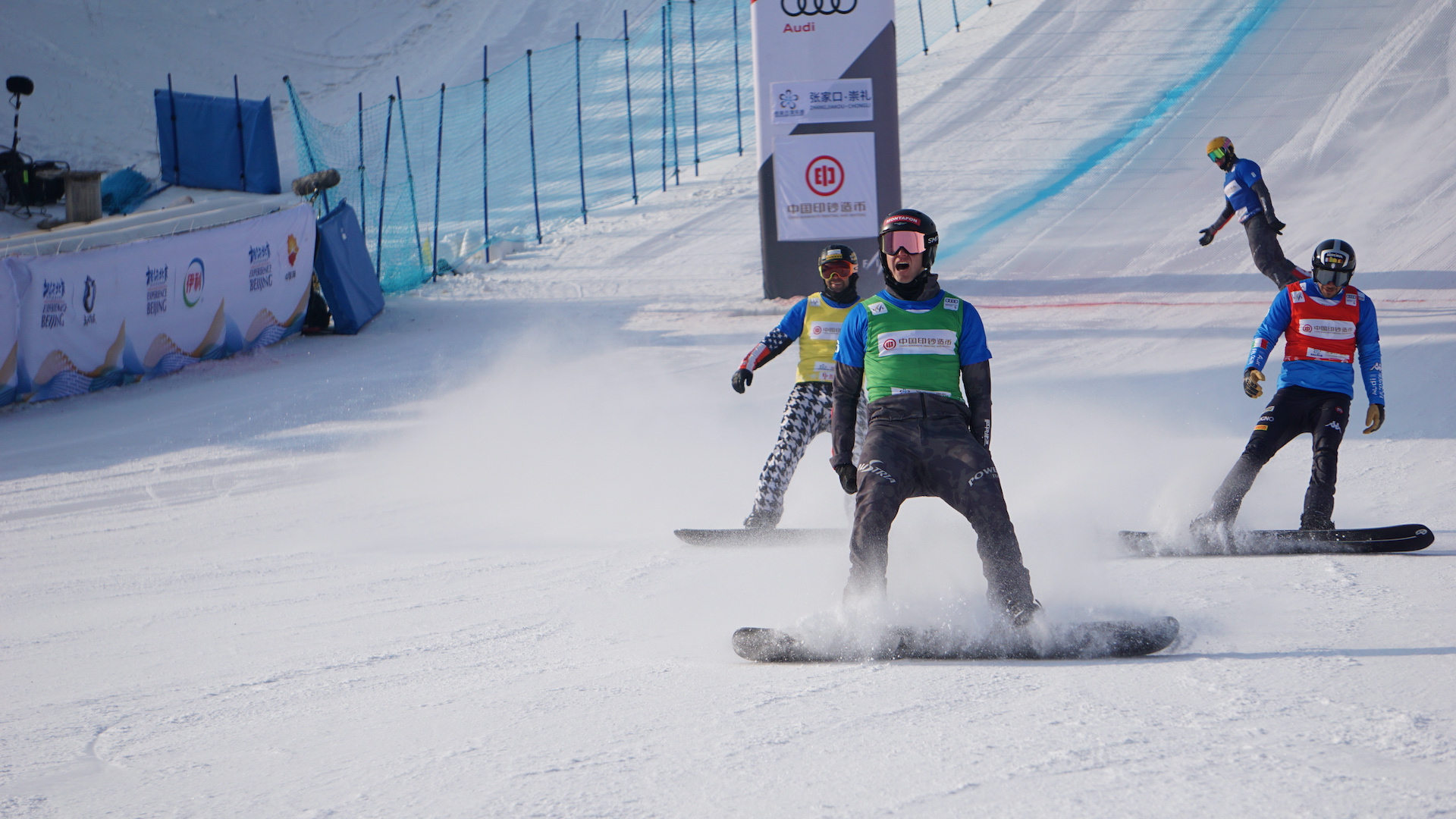 Three snowboardcross competitors cross the finish line. 