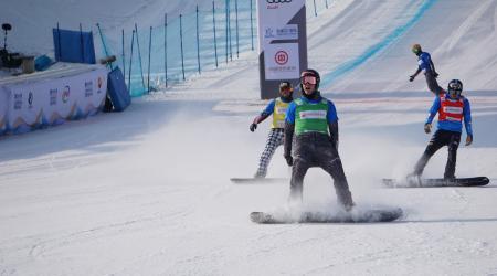 Three snowboardcross competitors cross the finish line. 